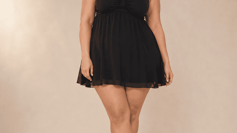 Woman with apple body shape wearing a black empire waist dress showing off her legs