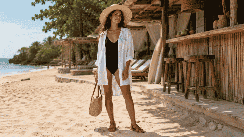 Flat lay of a 10-piece vacation capsule wardrobe in neutral tones with linen pieces, sandals, and a straw bag