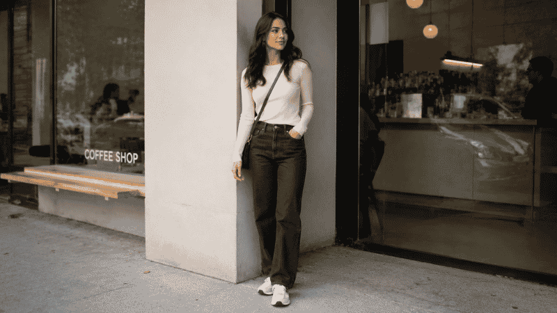 Woman in a casual coffee date outfit wearing dark jeans, fitted top, and clean white sneakers