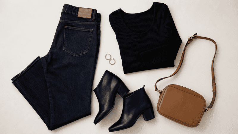 Flat lay of a quick date night outfit formula: dark jeans, black fitted top, ankle boots, gold hoops, and small bag