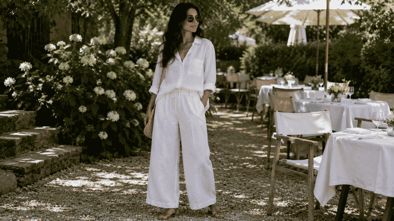 Woman in an outdoor brunch outfit wearing a white linen co-ord set and flat sandals at a garden brunch