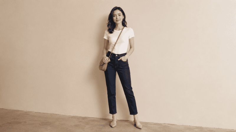 Petite woman in well-fitting high-rise dark wash straight-leg jeans with white fitted top and nude pointed-toe flats looking tall and confident