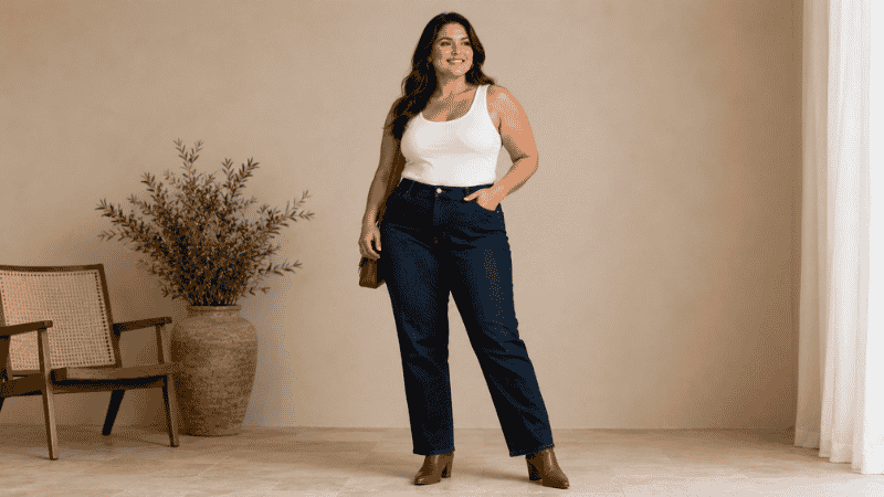 Curvy woman in high-rise straight-leg dark wash jeans with a tucked fitted top and ankle boots