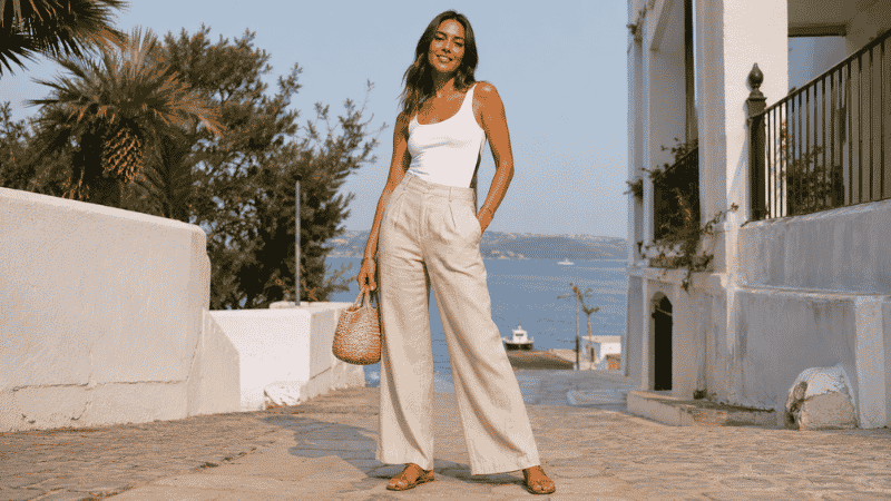 Woman in a chic linen pants outfit wearing wide-leg beige linen pants, white fitted tank, and flat sandals
