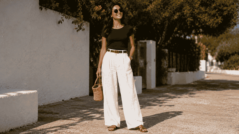 Woman in white linen pants outfit with a navy fitted top and flat sandals on a sunny day