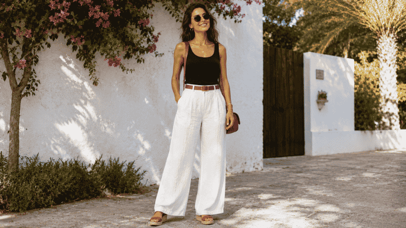 Woman wearing wide-leg white linen pants with a fitted navy tank top and wedge sandals