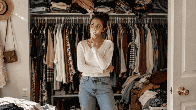 Overwhelmed woman looking at a cluttered overfull closet representing the problem capsule wardrobes solve