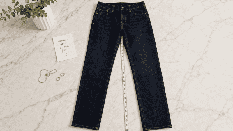 Flat lay showing a measuring tape alongside tall women's jeans illustrating long inseam length measurement