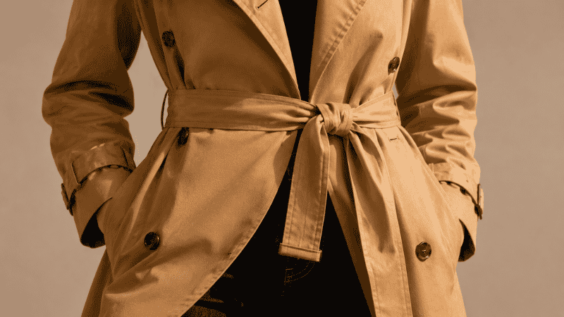 Close-up detail of a trench coat belt tied in a classic front knot at the natural waist showing the correct technique