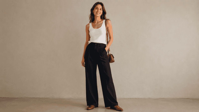 Woman wearing wide-leg dark trousers with a fitted white tank top French tucked showing the correct proportion formula